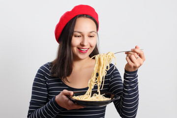 Young woman in a red beret eating spaghetti. On white.