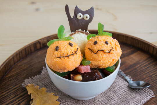 Halloween dessert in a white cup. It consists of ice cream in the form of ghost pumpkins and chocolate black cat. Creative food for the holiday and a good mood.