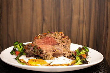 Roasted and seasoned meat with accompaniment of fried egg, brocolis, onion and tomato.
