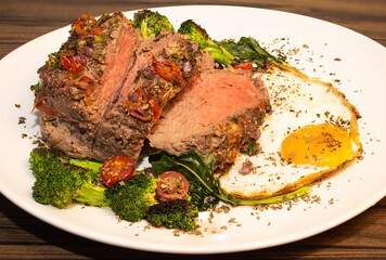 Roasted and seasoned meat with accompaniment of fried egg, brocolis, onion and tomato.