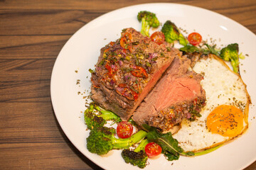 Roasted and seasoned meat with accompaniment of fried egg, brocolis, onion and tomato.