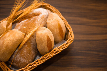 Australian and wholemeal bread in wicker basket on wooden background, with space for writing.Decorated with ear of wheat.