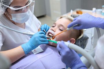 Fototapeta premium Dentist brushing the teeth of a little boy. Professional hygiene of the oral cavity. Concept of health care and disease prevention. Pediatric dentistry. Hands in protective gloves.