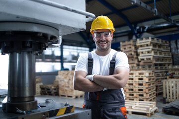 Portrait of factory worker with arms crossed standing by drilling machine in industrial plant.