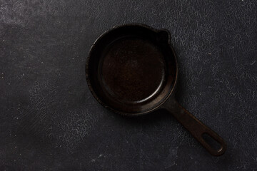 Empty black cast iron frying pan on a dark graphite background. Light linen towel.