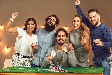 Group of excited friends celebrating successful game of poker at casino themed party