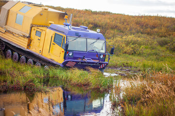 an all-terrain vehicle on tracks overcomes a swamp in the tundra