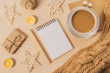 Obraz na płótnie Canvas Cozy home still life: a white cup with coffee, a chunky knit scarf, a notebook with a pencil, candles and gifts. The concept of the coming winter, christmas eve and new year. Warm shades, close-up.
