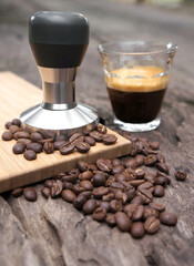 Coffee Espresso and Tamper or coffee press with coffee beans on a wooden table.