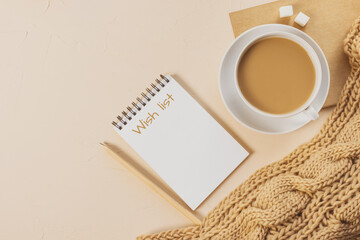 Cozy home still life: a white cup with coffee, a chunky knit scarf, a notebook with a pencil. Wish list. The concept of the coming winter, christmas eve and new year. Warm shades, close-up.