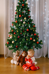 Obraz na płótnie Canvas Small child is snacking on an apple in front of a Christmas tree with her stuffed toys under it