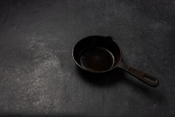 Empty black cast iron frying pan on a dark graphite background. Light linen towel.