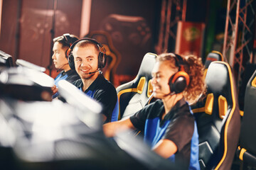Happy young guy, male gamer wearing headphones looking mixed race girl sitting close to him, cybersport team participating in eSport tournament