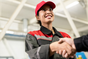 Young cheerful female engineer in workwear looking at colleague or foreman