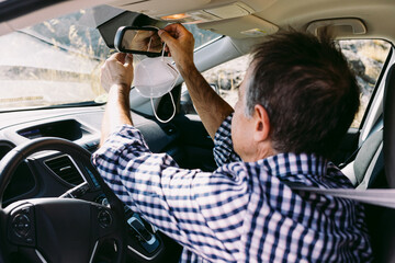 Mature man placing protective mask on rear view mirror