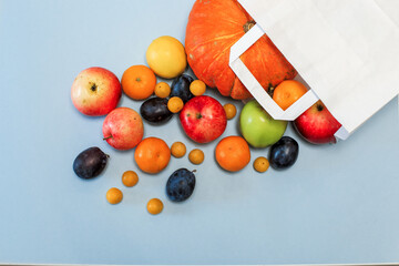 Package with scattered colored fruit on a blue background. Plums, tangerines, lemon, apples, pumpkin. Shopping in the store
