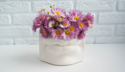 Autumn or spring bouquet of violet garden flowers in modern lips shaped vase. Modern art beauty concept.