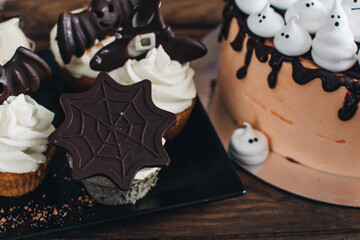 Sweets for halloween party on a wooden table. Halloween style party, candy bar and decorations with pumpkins. Halloween cake, cupcakes and muffins with chocolate. 