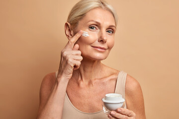 Close up shot of middle aged beautiful woman applies anti aging cream on face undergoes beauty...