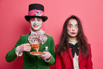 Photo of girl ghost has scarying makeup and pleased crazy hatter in costume drinks tea on party....