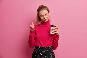 Rude furious woman shows middle finger looks in dissatisfied expression drinks coffee to go...