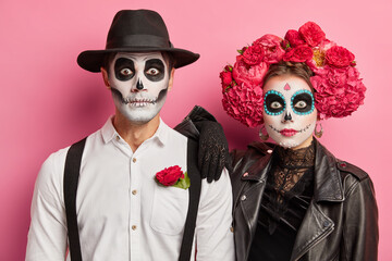 Day of dead concept. Bridal couple with vivid makeup typical mexican costumes pose against pink...