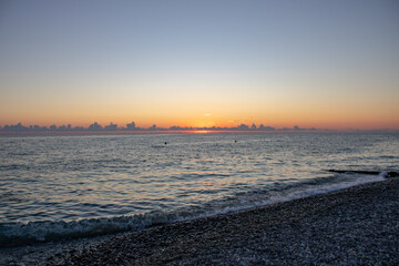 A beautiful panoramic view of the sunset over the Sochi sea with pink-blue clouds and a view of the pebble beach.