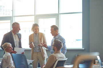 Powerfully successful team. Group of multiracial business people in classic wear discussing work and sharing ideas while standing in the modern office or coorking space