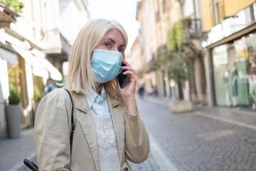 Masked woman talking on the phone while walking in a city street, coronavirus concept