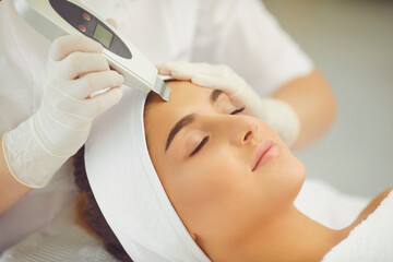 Naklejka premium Relaxed woman getting ultrasound apparatus facial cleaning from cosmetologist