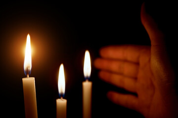 Someone's hand covering the candle in a dark design for the background, the candle in the dark symbolizes the Christian faith. Candle burning in the dark with the light.