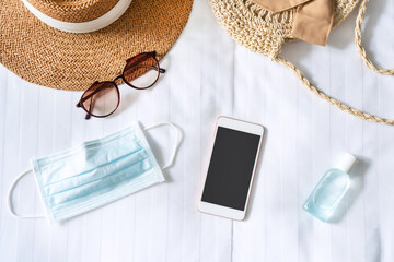 Top view of smartphone, travel accessories, surgical mask and sanitizer gel on bed in hotel room....