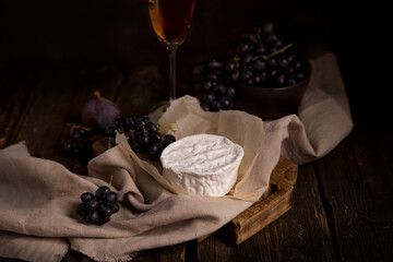 camembert cheese, glass of wine, figs and grapes on a dark wooden table. dark background. Still life with brie cheese. Copy space.