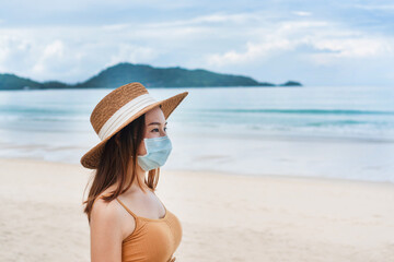 Beautiful young Asian traveler woman with protective face mask at the beach. New normal, health care, travel and holiday concept