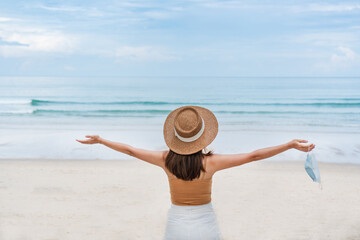 Beautiful young Asian traveler woman take off protective face mask at the beach. New normal, health...