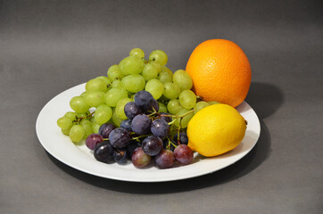 Lots of healthy food. Fruit on a white plate on a gray background. Beautiful still life of fruit.