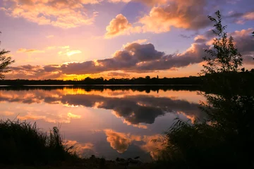 Foto op Canvas Amazing sunrise in rural scene. Symmetry of the sky in a lake at sunset. Clouds reflecting on the water. Quiet relaxing scene with a beautiful colorful cumulonimbus. Silhouette of vegetations. © Bruno