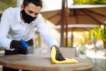 Cleaning and disinfection of table to prevent COVID-19. Waiter in  protective face mask and gloves  disinfecting tables at outdoor cafe to preventing the spread of coronavirus in quarantine city.