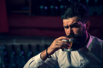 Handsome bearded man enjoying whiskey in bar. Hipster drinking a brandy in bar. Brutal guy drinking alcohol.