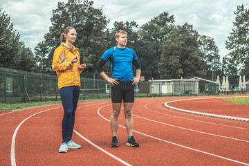 Young Caucasian woman and man observing athletic track while taking a training break