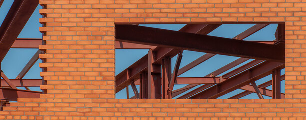 A window in an unfinished red brick building, through which the internal supporting metalwork is visible.