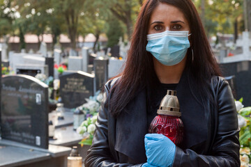 A woman wearing a protective mask against the coronavirus COVID-19 SARS-CoV-2 holds a candle in her...