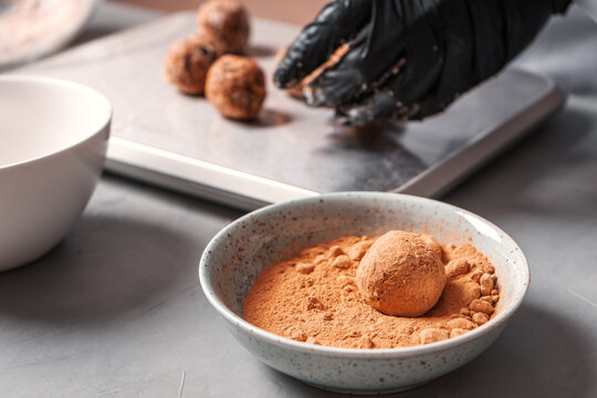 A Black-gloved Cook Prepares Date Sweets And Rolls Them In A Carob