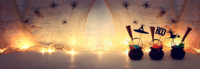 holidays image of Halloween. Witcher cauldron, broom, candies and spiders over white wooden table