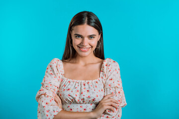 Obraz premium Young smiling woman looking to camera. Portrait of cute beautiful girl in floral dress on blue studio wall background.