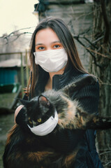 Girl Holding Cat in Hands on the street, medical mask because of Coronavirus or air pollution or...