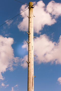 Telegraph pole against a blue sky with white clouds. Old weathered post with foot grips. 