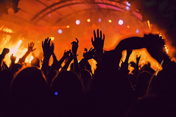 Fototapeta na wymiar Abstract blur atmosphere: happy people enjoying outdoor music festival concert, raised up hands and clapping of pleasure, active night life concept, play of light and shadow on the stage
