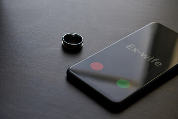 The black smartphone that the ex-wife is calling is lying on a dark surface next to the wedding...