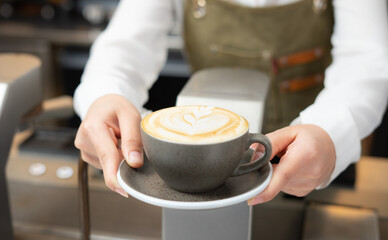 Close up shot of barista girl hands serving nice hot latte art coffee.